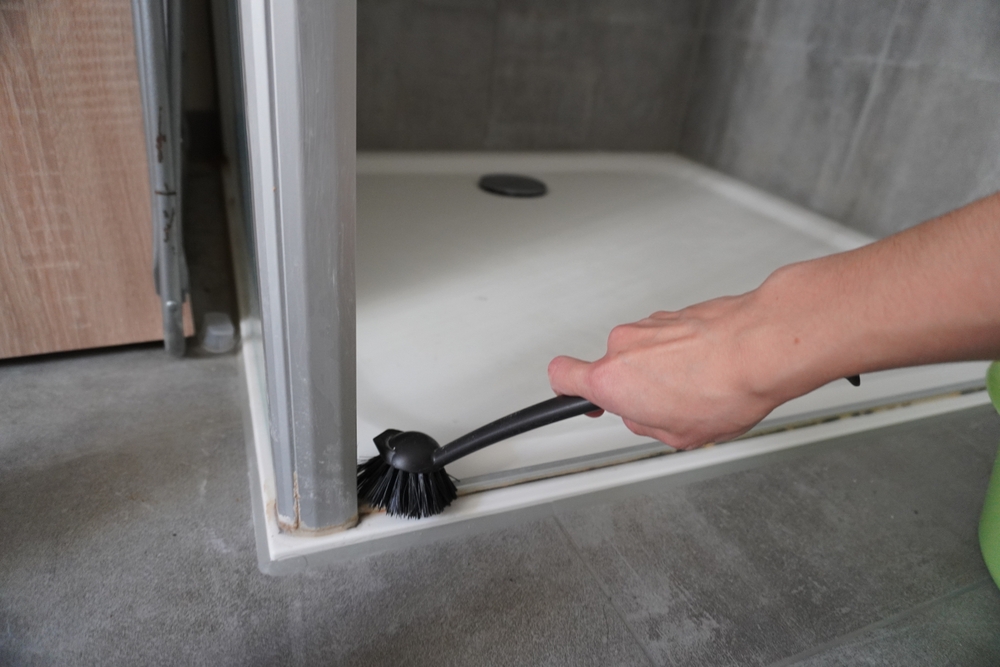 woman,hand,cleaning,shower,door,frame,with,brush,on,tiled